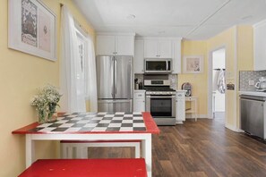 Une cuisine avec des meubles blancs, des appareils en acier inoxydable, une table à carreaux et un banc rouge.