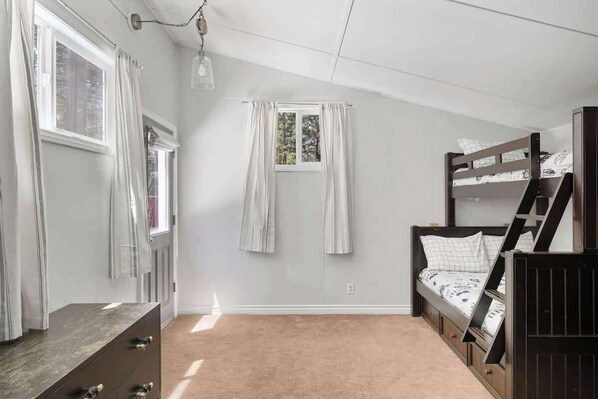 Une chambre avec un lit superposé, une commode, une fenêtre avec des rideaux et un luminaire au plafond.