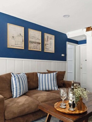 A living room with a brown sofa, two blue and white striped pillows, and a wooden coffee table with wine glasses and a bottle.