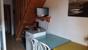 A compact room with a wooden sloped ceiling, a small kitchenette with a refrigerator, a microwave, and a coffee maker. A television is mounted on the wall above a small table. - 4-person apartment (Picherande)