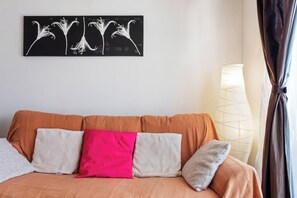 A room with a brown sofa, two pillows, a wall-mounted artwork, and a floor lamp.