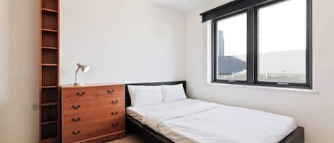 Un dormitorio con cama, cómoda de madera, escritorio y ventana.