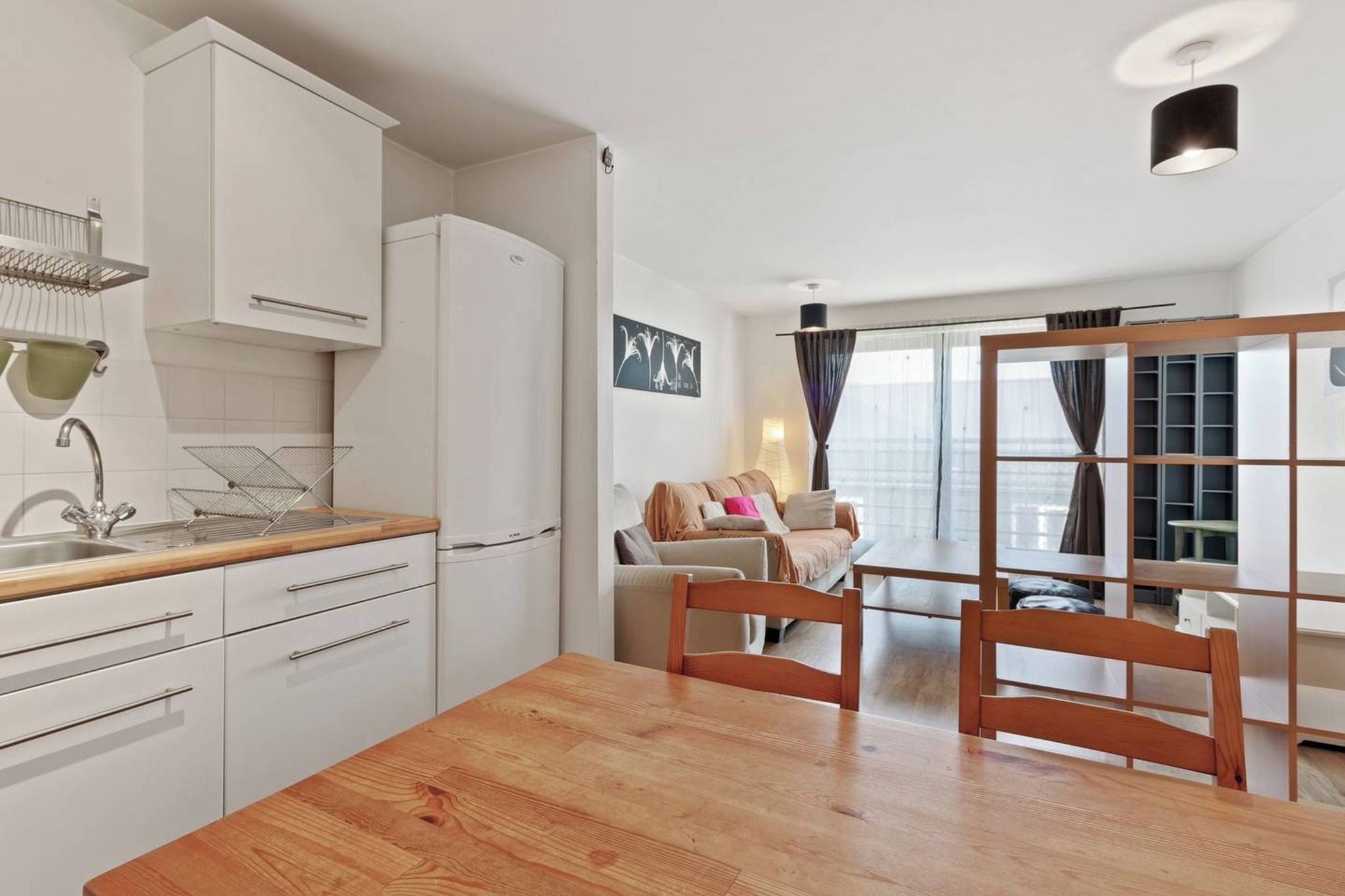 A modern kitchen with white cabinets, a wooden countertop, and a dining area with a wooden table and chairs.
