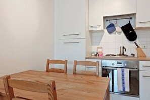 A compact kitchen with a wooden table and chairs, a built-in oven, and a hanging pot rack.