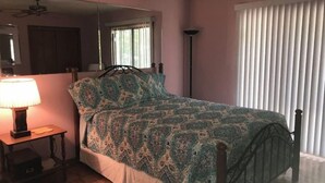 A bedroom with a bed, a nightstand, a lamp, a mirror, a ceiling fan, and a window with blinds. - Nature at it's Best (Old Fort)