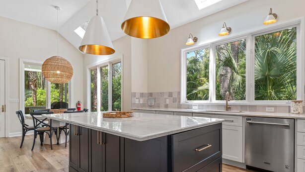 Een moderne keuken met een groot keukeneiland, hanglampen en grote ramen met uitzicht op groen.