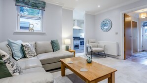 A modern living room with a sofa, coffee table, and a view of the kitchen. - Jasmine Cottage (Chipping Campden)