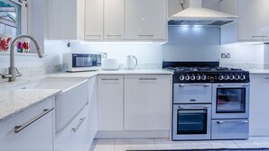 A modern kitchen with white cabinetry, a built-in microwave, a gas stove, and a range hood. - Jasmine Cottage (Chipping Campden)