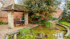 A rustic garden with a pond, a wooden bench, and a brick structure. - Jasmine Cottage (Chipping Campden)