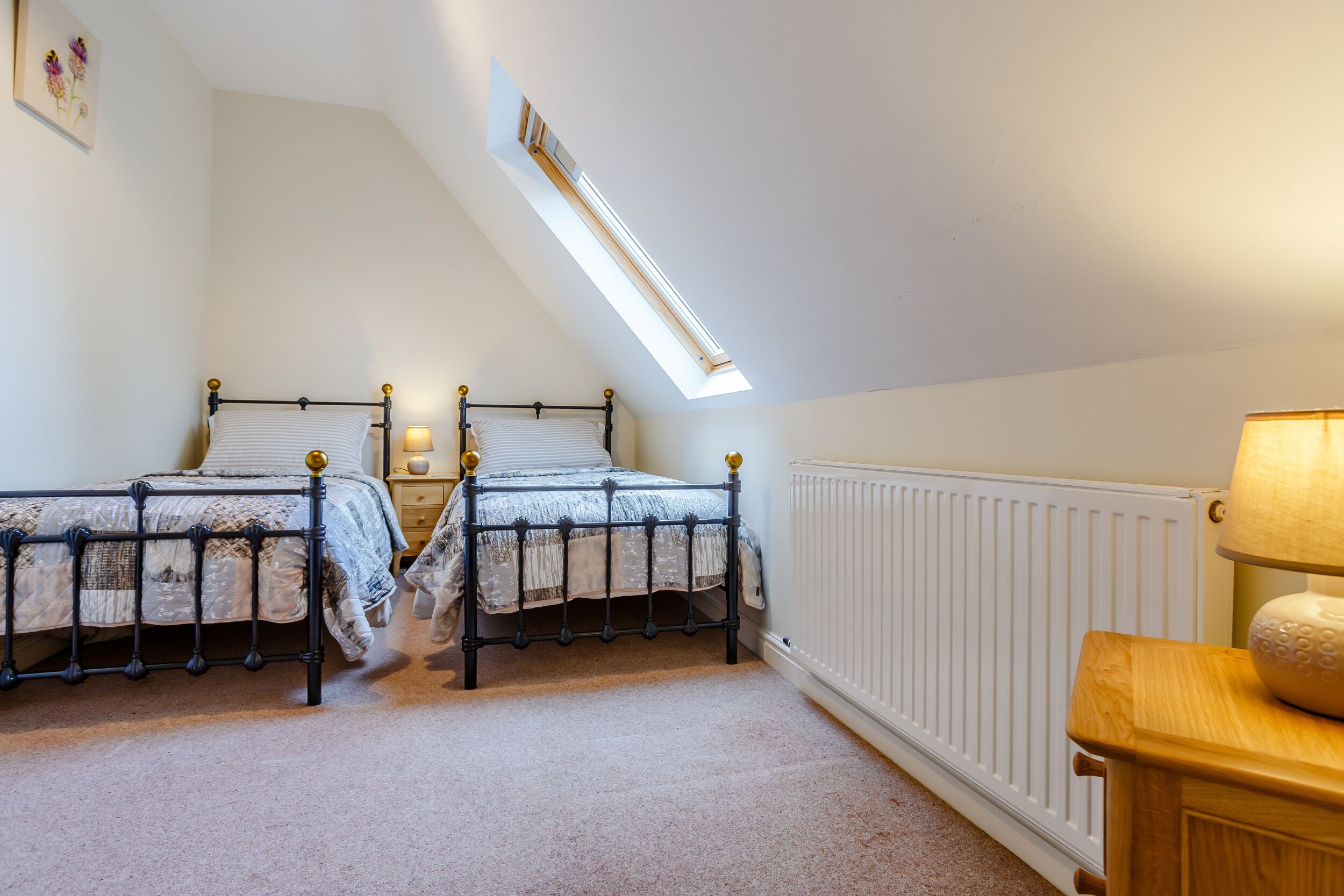 A bedroom with two beds, a skylight, a radiator, and a wooden nightstand.