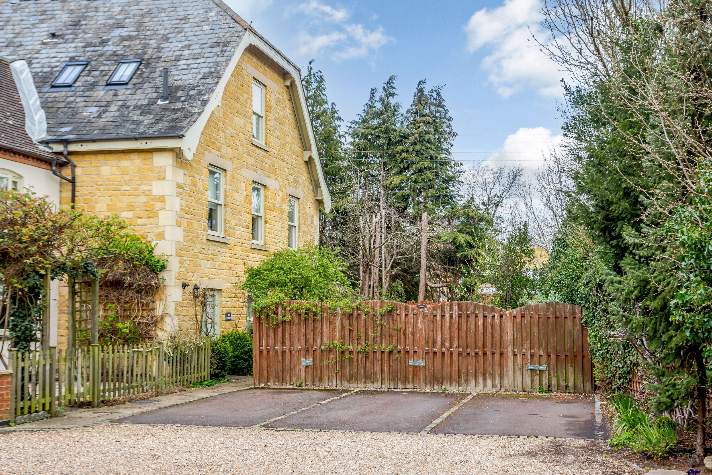 A residential property with a stone facade, a wooden fence, and a gravel driveway.