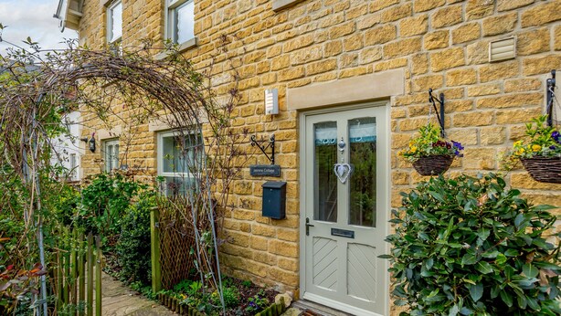 A stone building with a white door, a mailbox, and hanging flower baskets. - Jasmine Cottage (Chipping Campden)