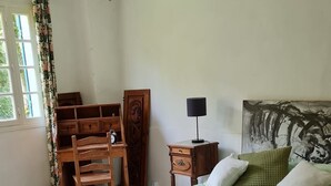 Makuuhuone, jossa on sänky, työpöytä, tuoli, yöpöytä ja ikkuna, jossa on verhot.