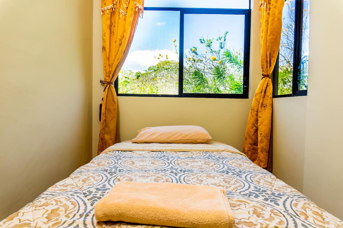 Uma cama de solteiro com roupa de cama estampada, um travesseiro e uma toalha dobrada.