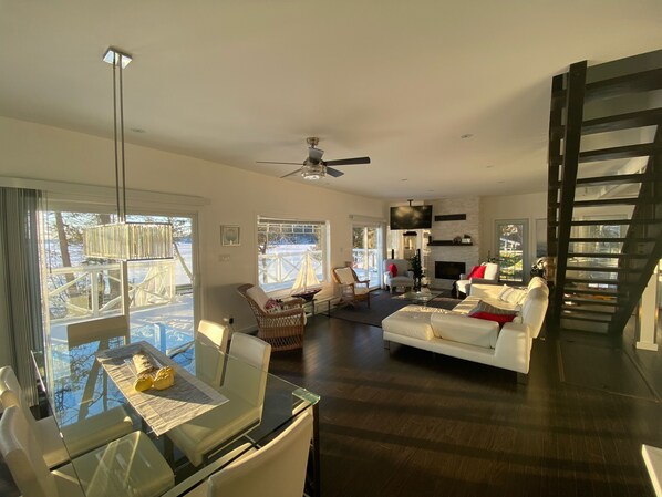 A spacious living room with a fireplace, a dining area with a glass table, and a staircase.