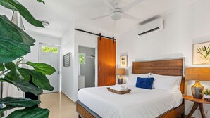 Une chambre moderne avec un grand lit, un ventilateur de plafond et une porte coulissante donnant sur une salle de bain.