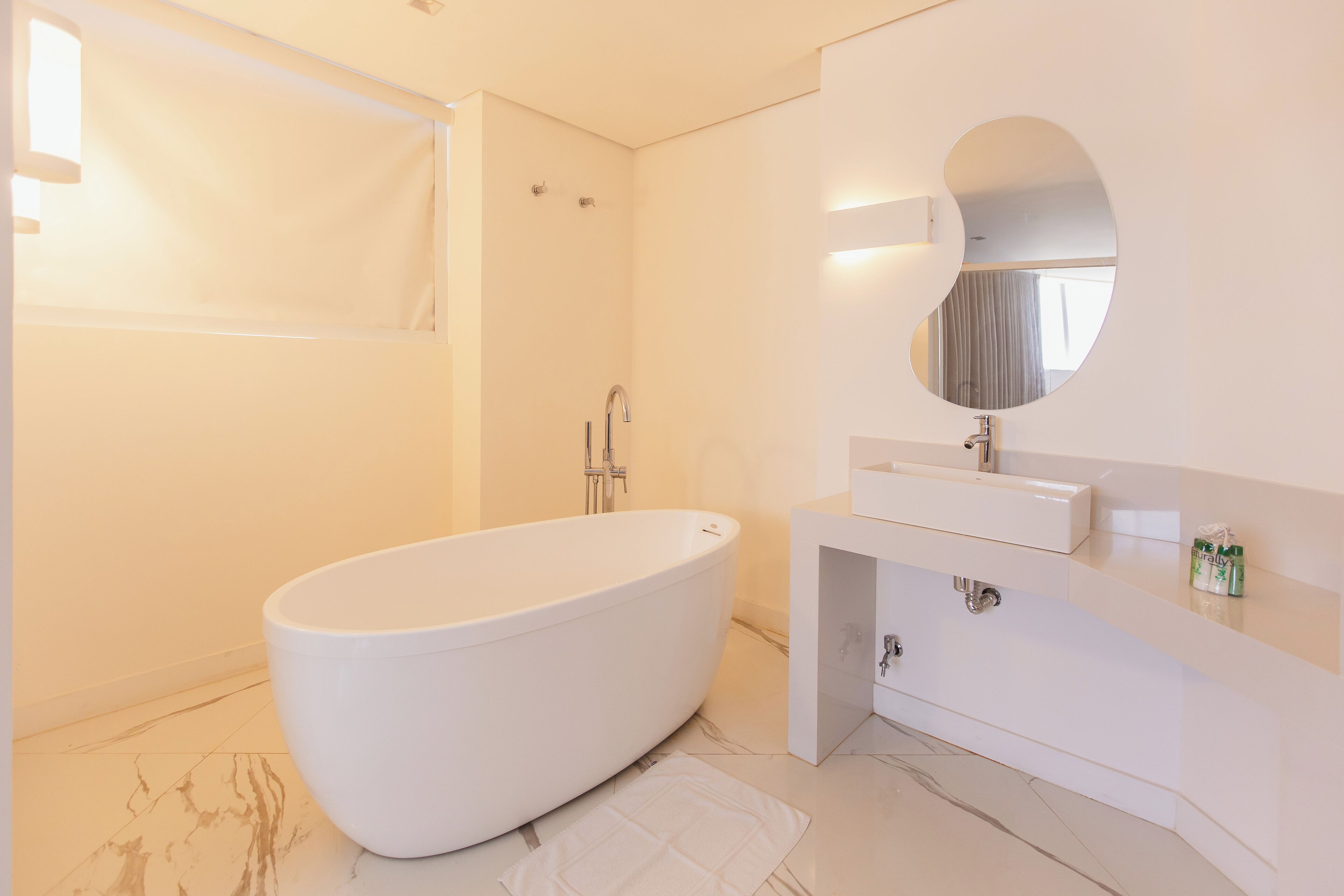 A modern bathroom with a freestanding bathtub, a round mirror, and a white vanity.