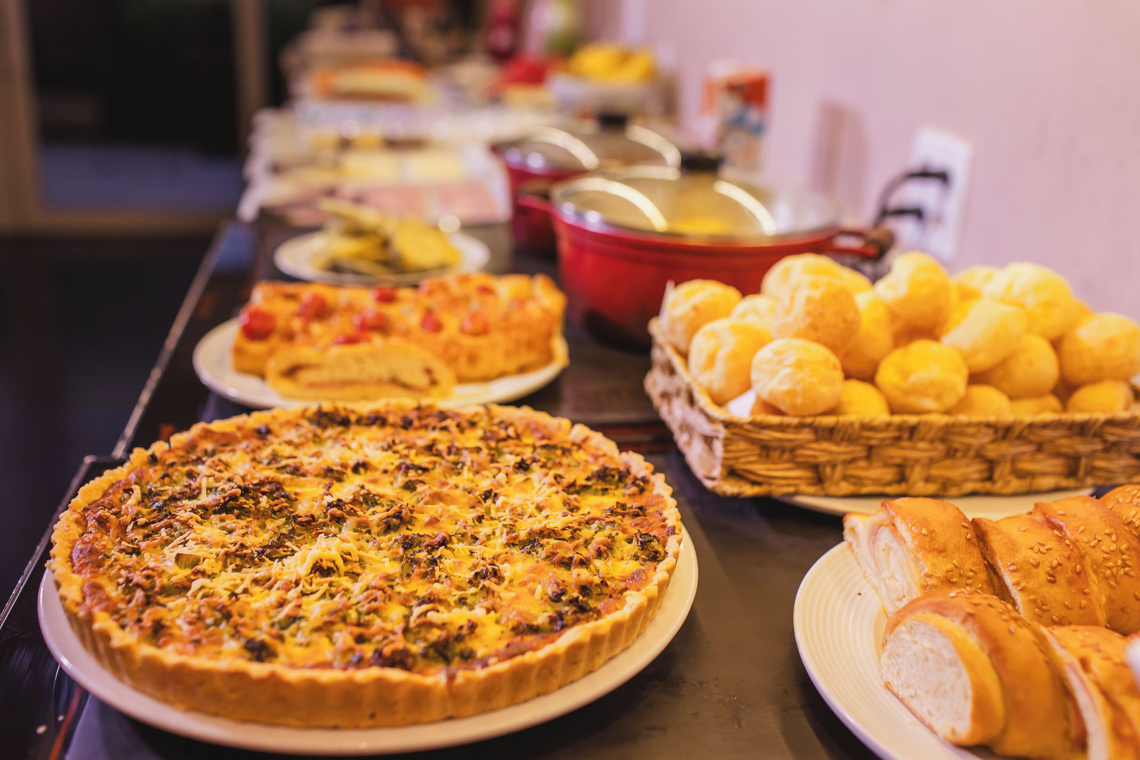 A buffet table with various dishes including a quiche, a pizza, and bread rolls.