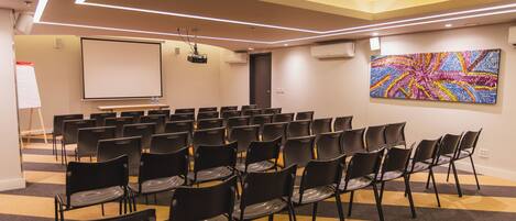 A conference room with rows of chairs, a projector screen, and a colorful abstract painting on the wall.