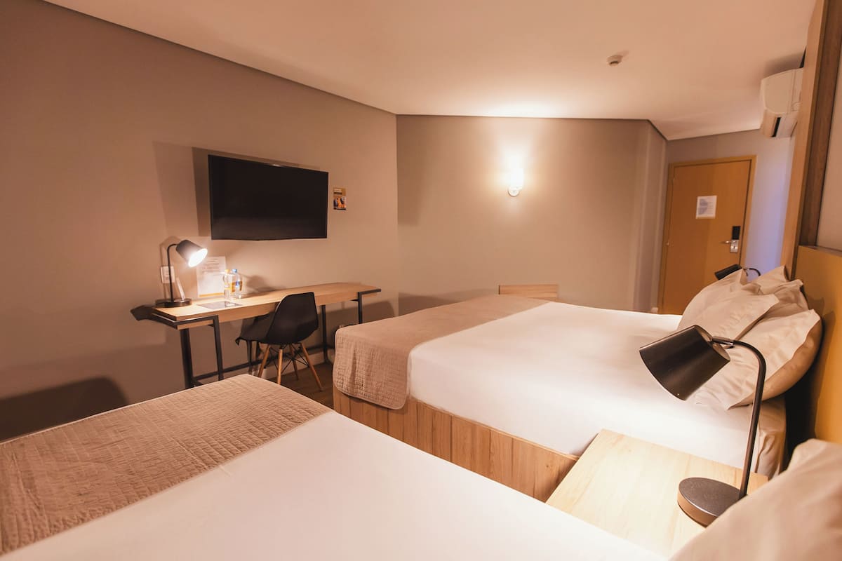 Habitación de hotel con dos camas, un escritorio, una silla, un televisor montado en la pared y una puerta.