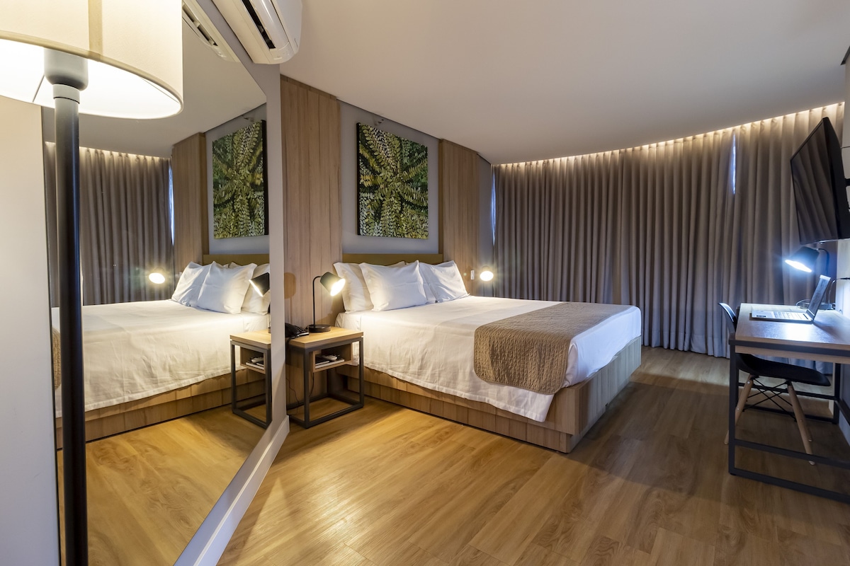 A modern hotel room with two beds, a desk, and a mirror reflecting the room.