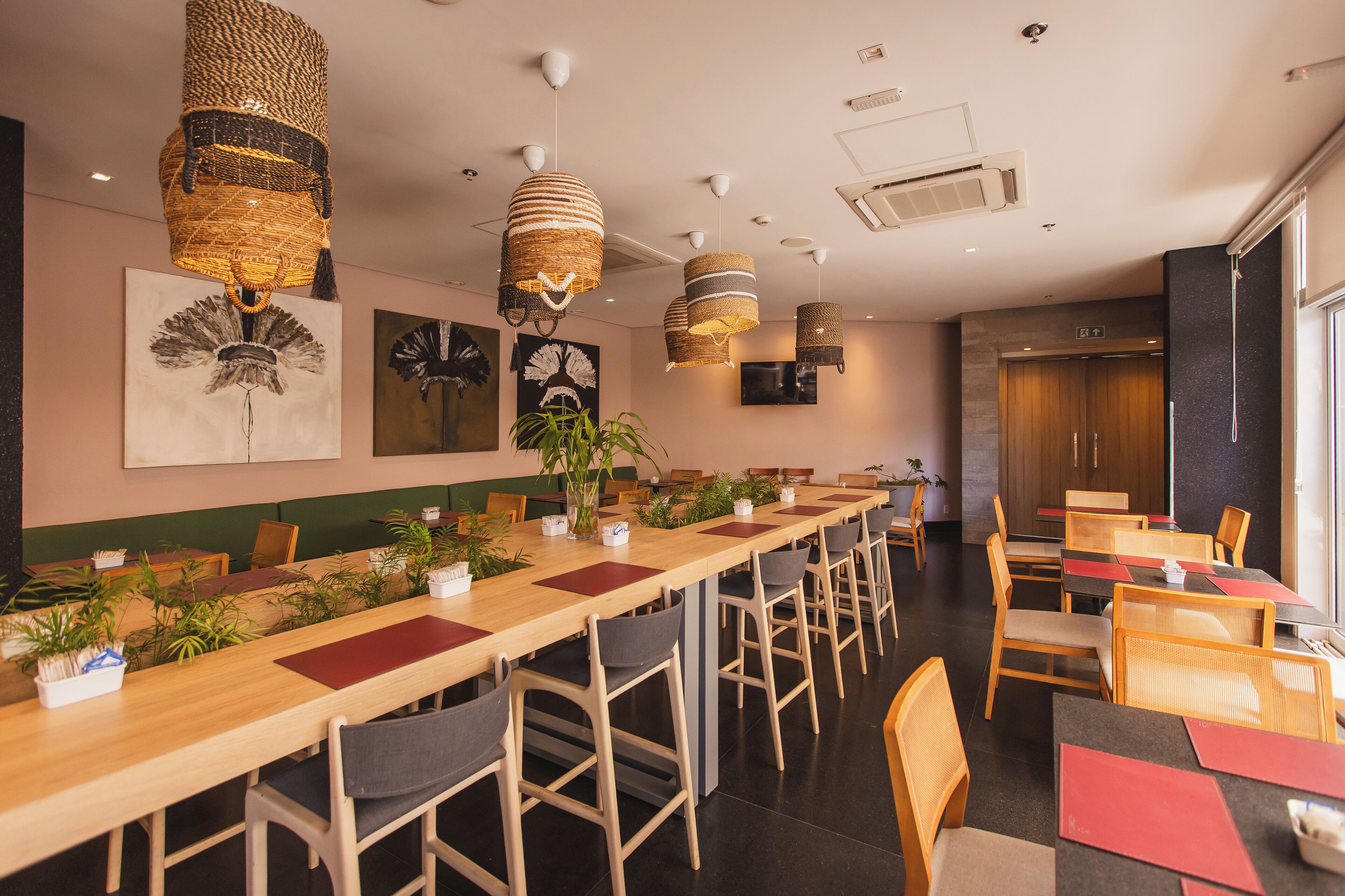 A restaurant with long wooden tables, wicker hanging lamps, and potted plants.