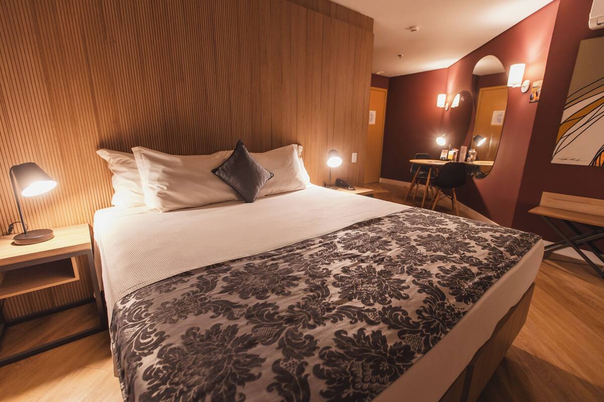 Una habitación de hotel con cama, lámparas de noche, escritorio y una silla.