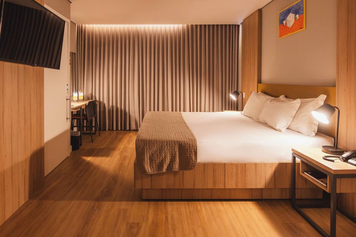 Una habitación de hotel con cama, mesita de noche, lámpara y un escritorio con silla.