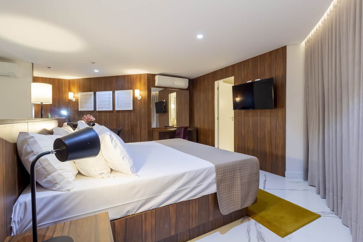 Una habitación de hotel moderna con cama, lámpara de noche, televisor montado y paneles de madera.