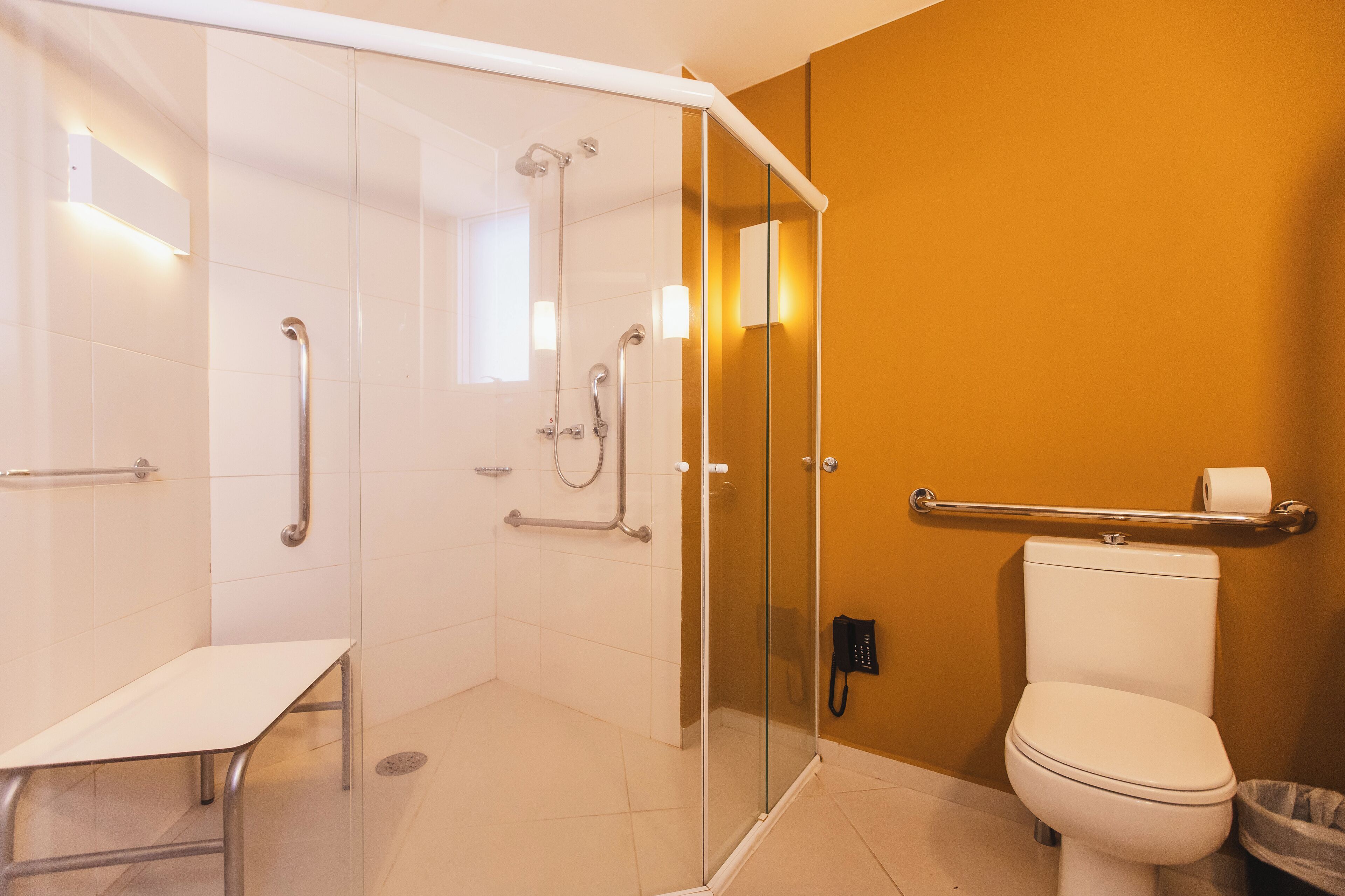Une salle de bain moderne avec une douche à parois de verre, des toilettes blanches et un banc.