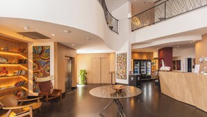 Un moderno vestíbulo de hotel con una mesa redonda central, área de descanso y una recepción.