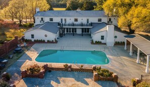 A large house with a swimming pool, covered patio, and a brick wall surrounding the pool area.