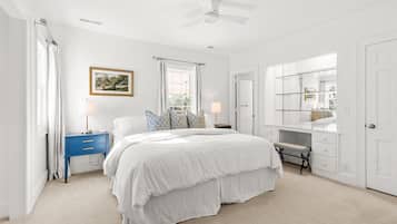 A bedroom with a bed, a nightstand, a dresser, a ceiling fan, and a window with curtains.
