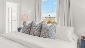 Een slaapkamer met een bed, een nachtkastje met een lamp en een raam met gordijnen.