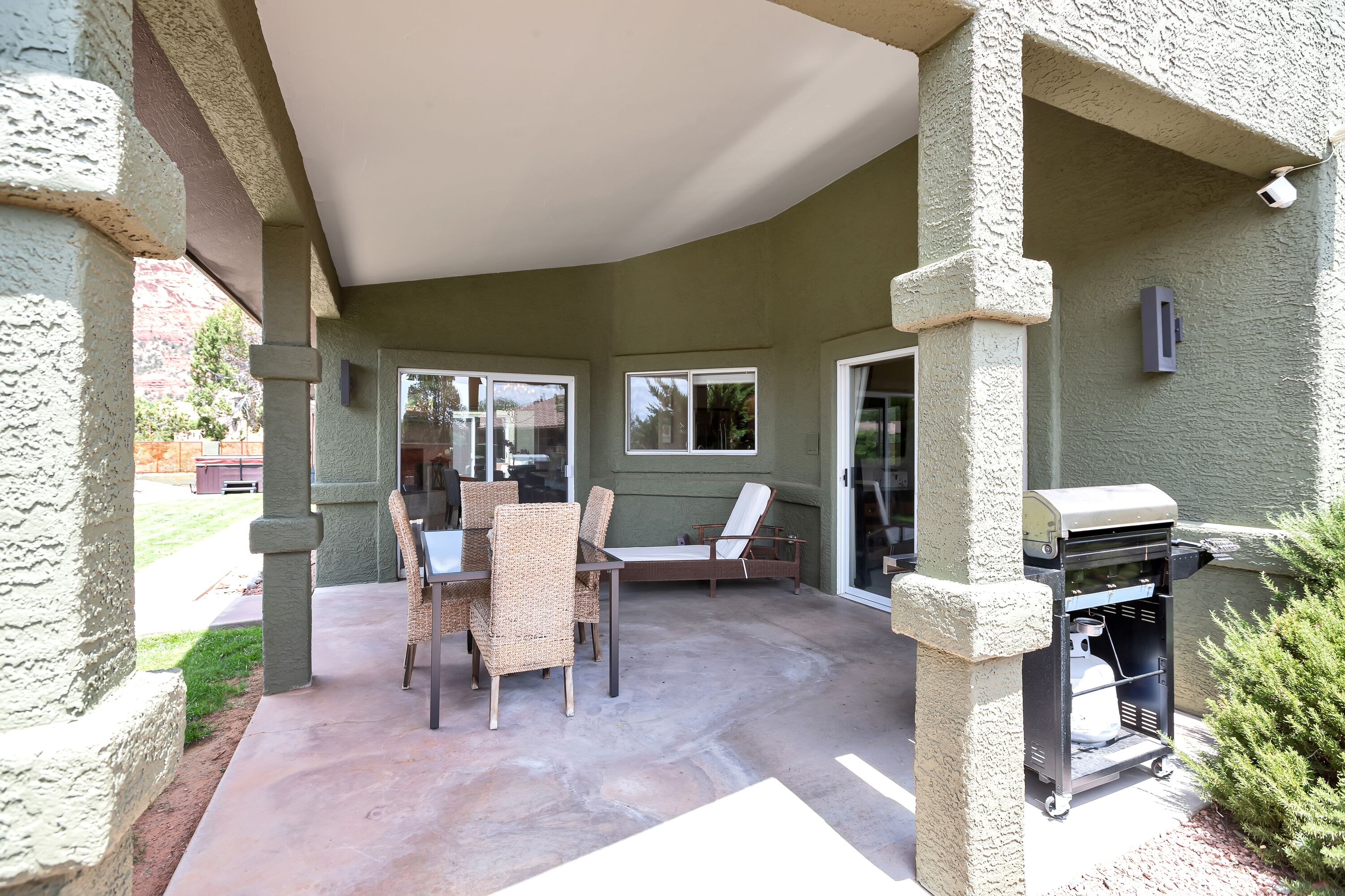 An outdoor patio with a covered seating area, a grill, and a table with chairs.