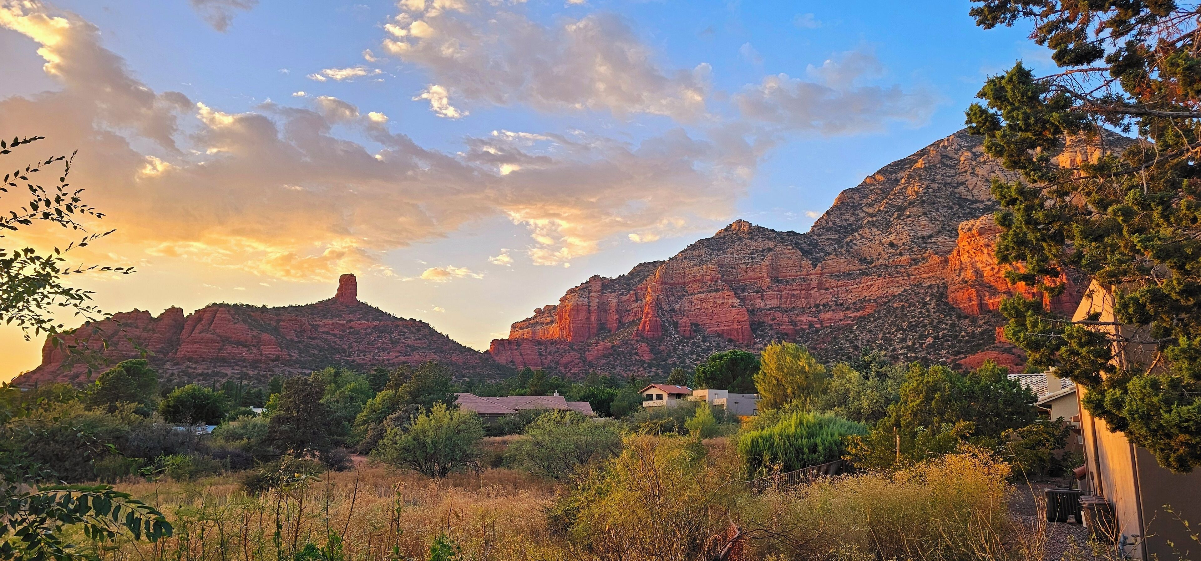 A mountainous landscape with a small cluster of buildings, likely a resort or lodge, surrounded by greenery and under a partly cloudy sky.