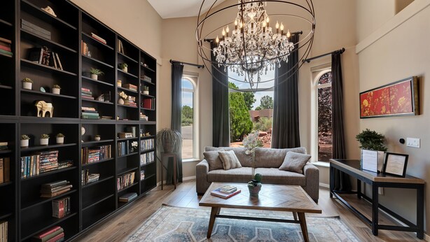 Uma sala de estar ampla com uma grande estante de livros, um lustre, um sofá e uma mesa de centro.
