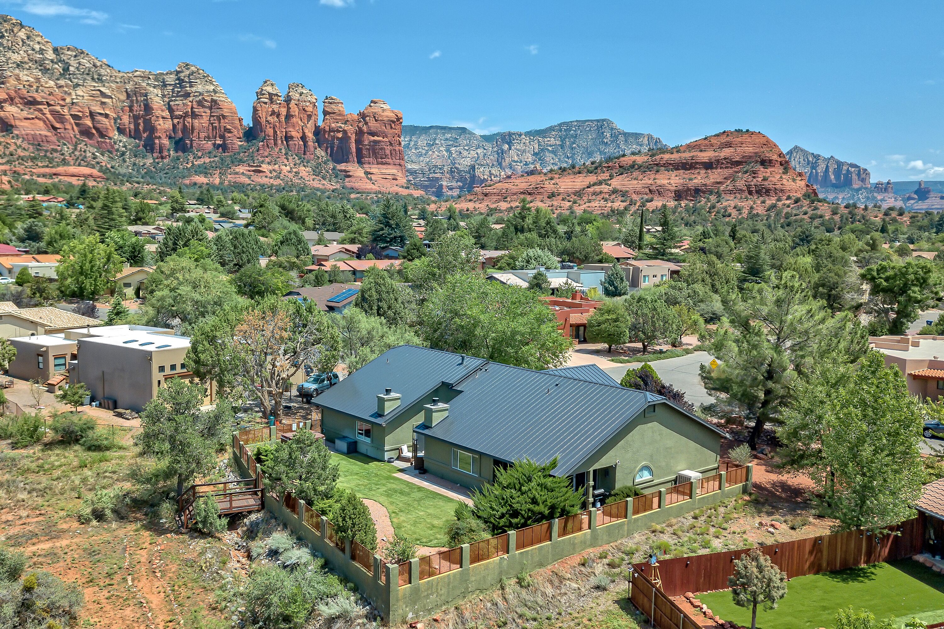 A residential area with houses surrounded by greenery and red rock formations in the background.