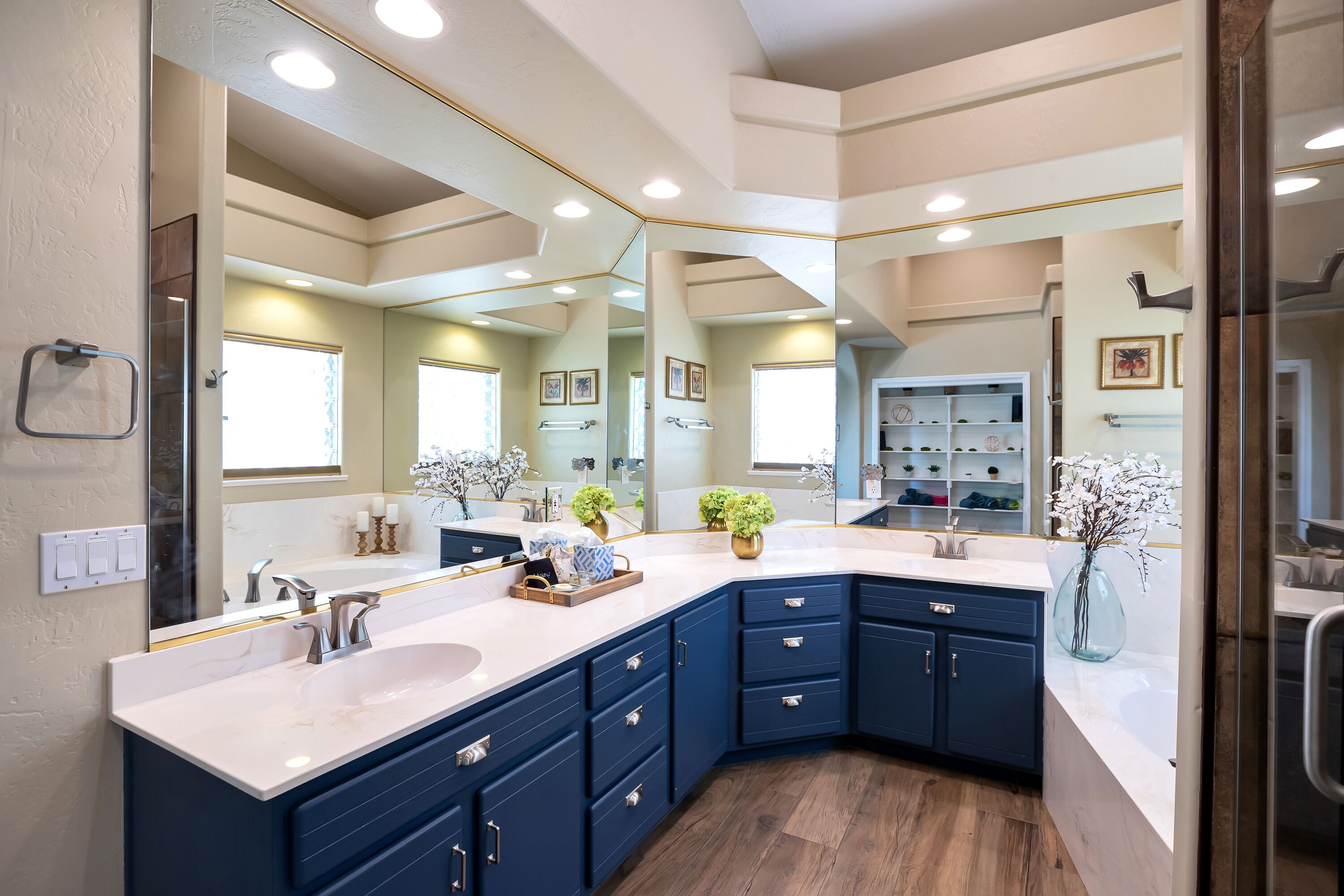 A modern bathroom with a large mirror, dark blue cabinets, and a white countertop.