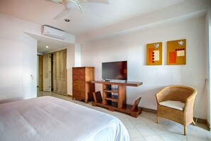 Una habitación de hotel con una cama, un televisor sobre un soporte de madera, una silla de mimbre y una obra de arte en la pared.