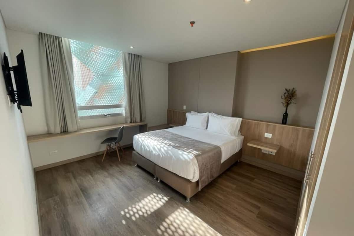 A modern hotel room with a large bed, a desk, and a window with curtains.