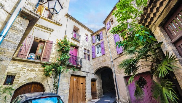 A narrow street with stone buildings, wooden doors, and balconies with purple shutters. - Beautiful apartment T3, private parking "Au logis de Pézenas". (Pézenas)