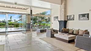 A spacious lobby with a large glass door leading to an outdoor area, a high stone pillar, and a seating area with sofas and a coffee table. - Waipouli Beach Resort | Spacious 2BD Retreat -Lazy River, Spa & Central Location (Kapaa)