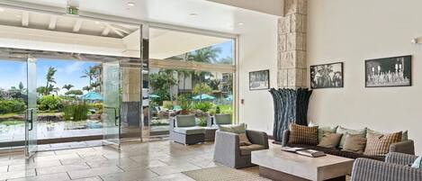 A spacious lobby with a large glass door leading to an outdoor area, a high stone pillar, and a seating area with sofas and a coffee table.