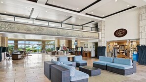 A spacious lobby with a high ceiling, a reception desk, seating area, and a view of the outdoors. - Waipouli Beach Resort | Spacious 2BD Retreat -Lazy River, Spa & Central Location (Kapaa)