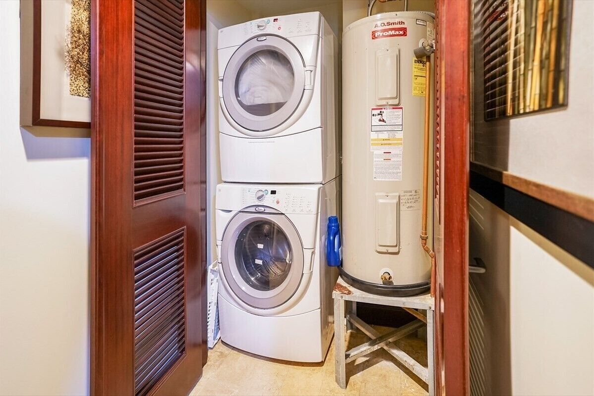 A laundry room with two stacked front-loading washing machines and a water heater.