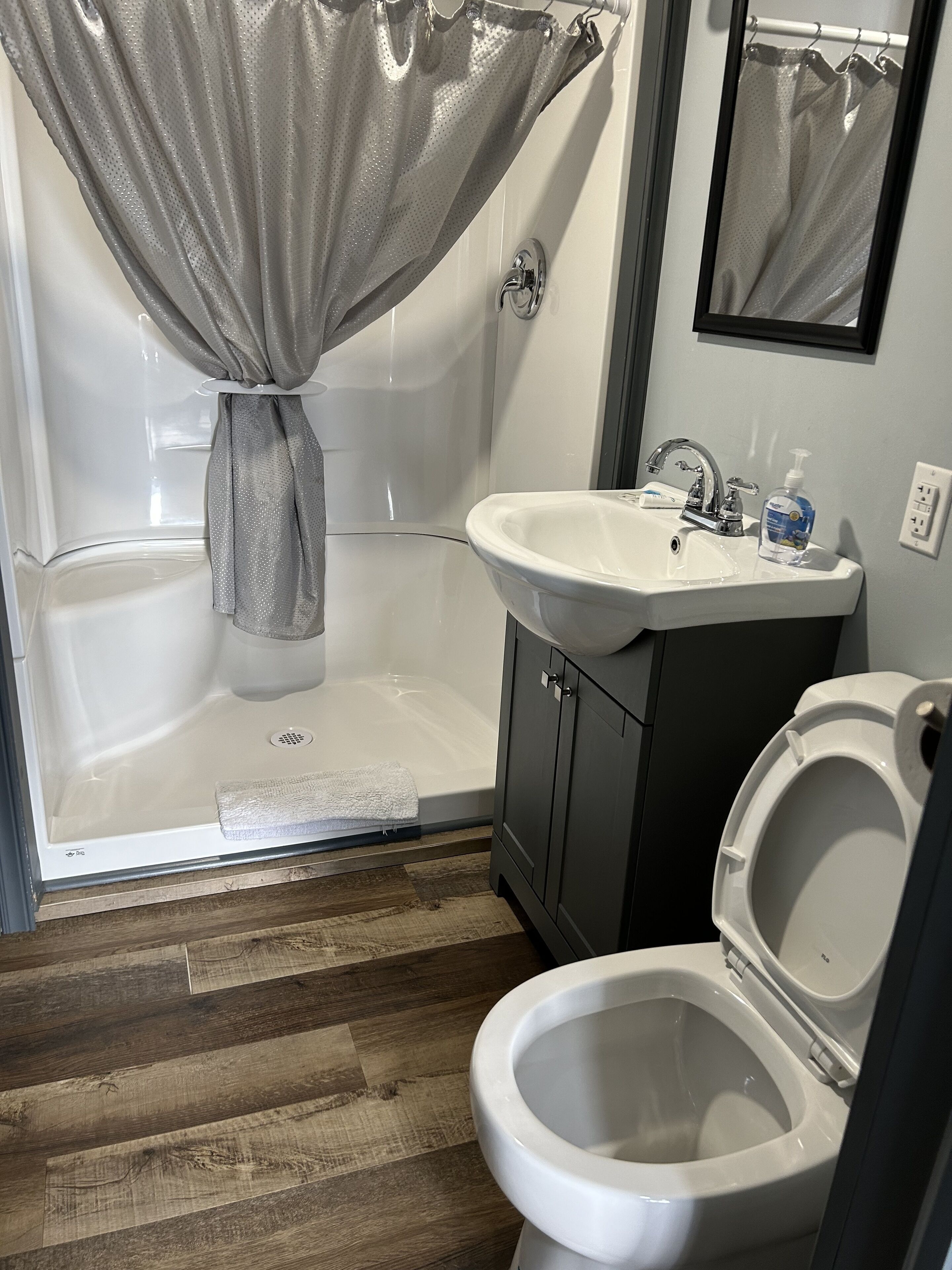 A bathroom with a shower, toilet, sink, and mirror.