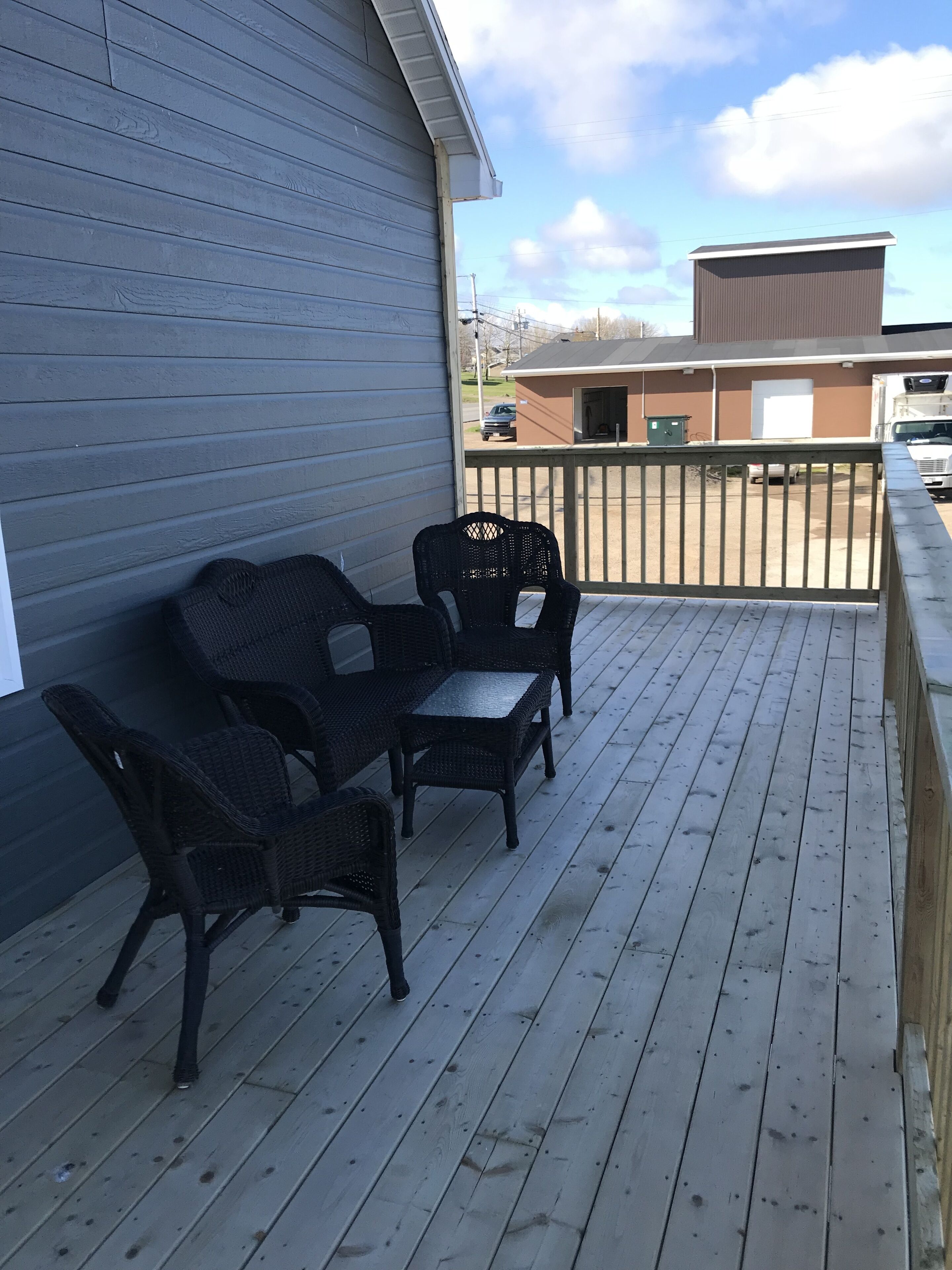 A covered outdoor area with a wooden deck, two wicker chairs, and a small table.
