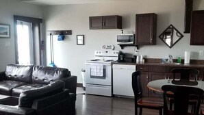A modern kitchen with dark wooden cabinets, a white stove, and a microwave. There's a dining area with a round table and chairs. - La Digue Suites  (Cheticamp)
