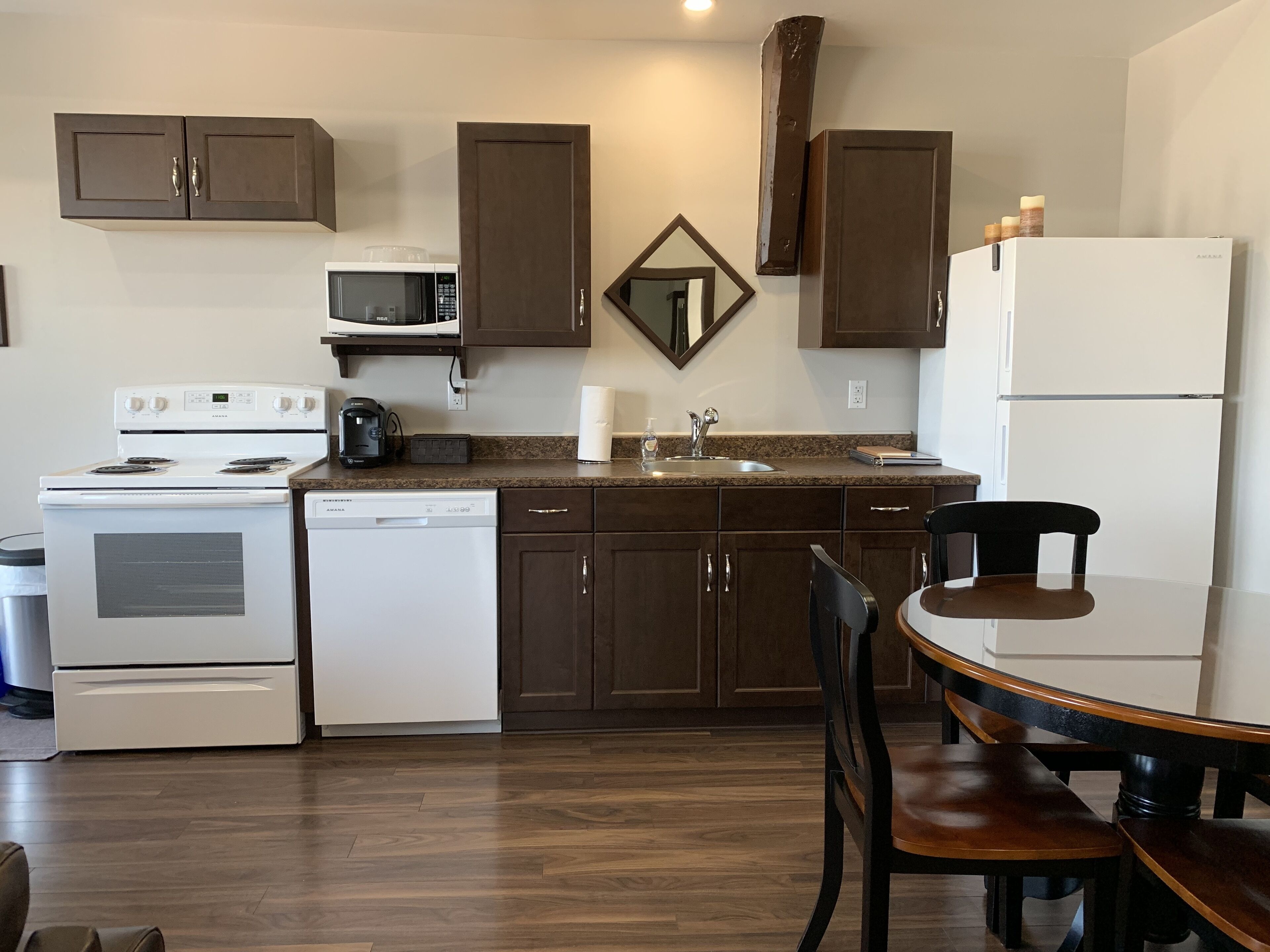 A modern kitchen with dark brown cabinets, white appliances, and a wooden dining table with chairs.